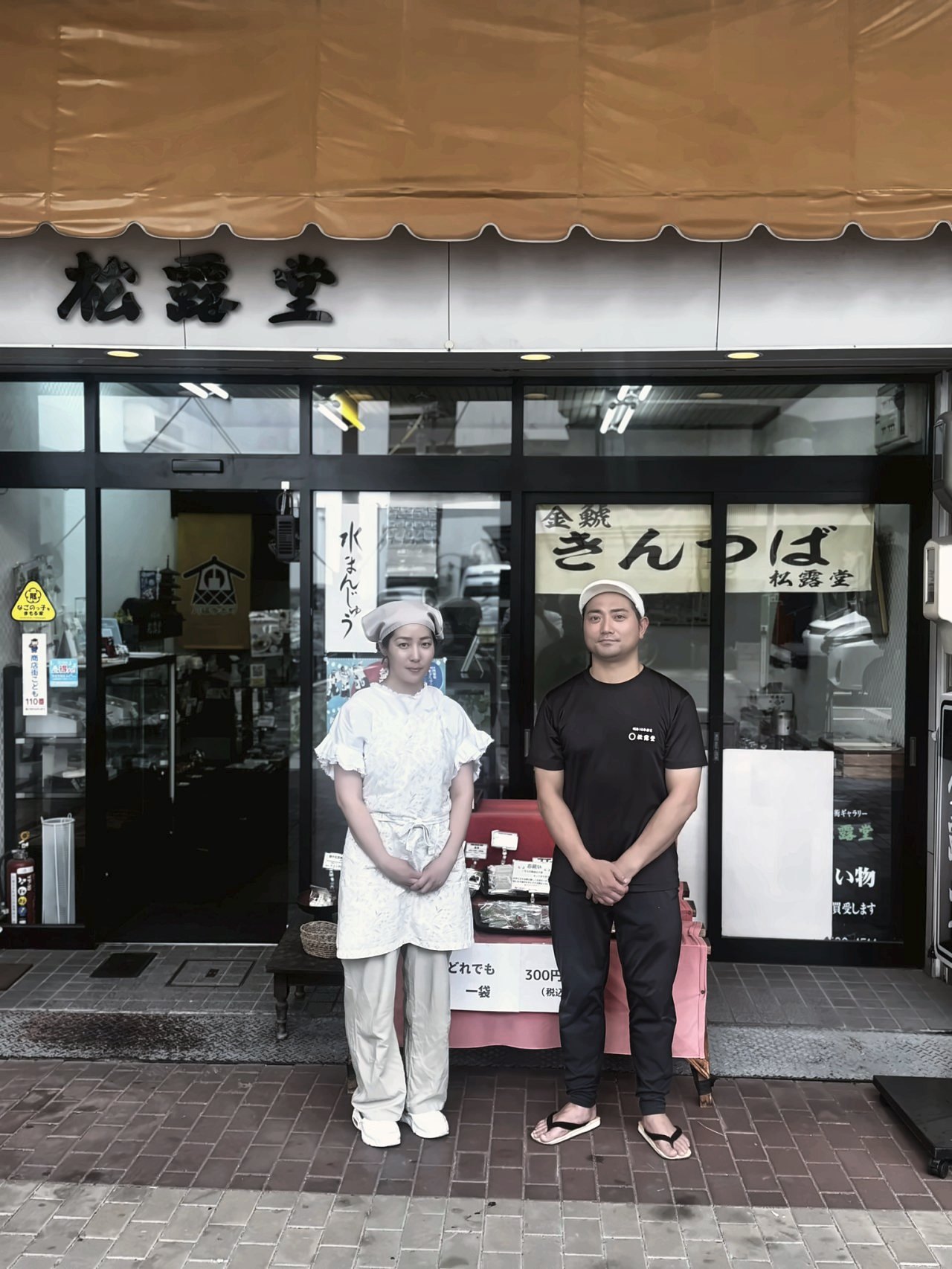 松露堂の暖簾の前に立つ、店主夫妻